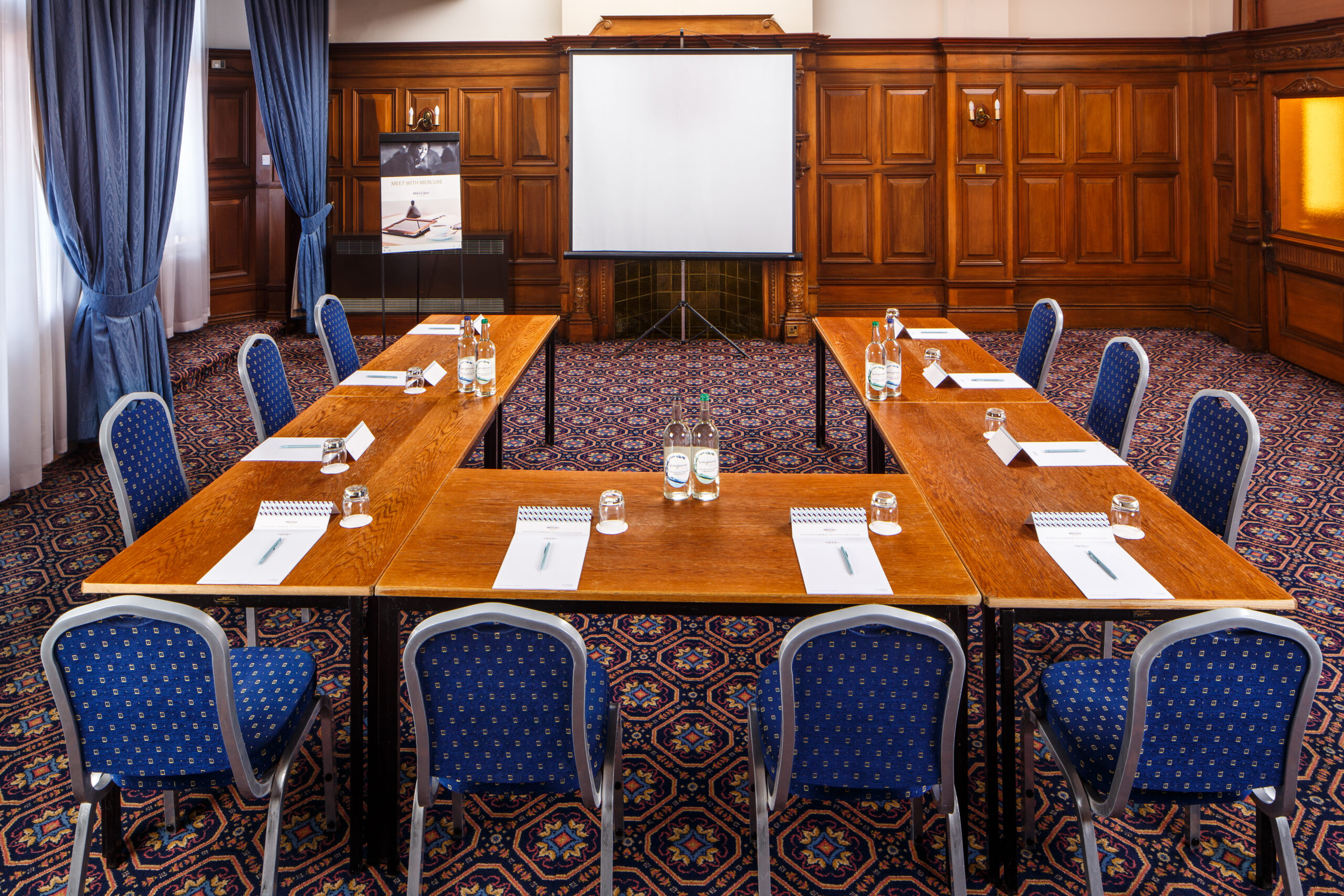 The long table seating 10 in The Boardroom at mercure gloucester bowden hall hotel ready for a meeting, with notepads and bottles of water on the table