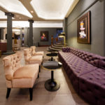 Velvet armchairs and a low leather chesterfield sofa with modern artwork on the wall and sweeping staircase in corner