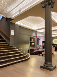 High backed velvet armchair in the lounge at Mercure Leicester The Grand Hotel, dramatic grey pillars and large staircase