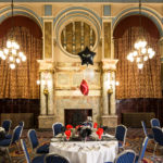 The King's Hall dressed for an event, with white tablecloths and black, white and red balloons. Large marble fireplace and chandeliers in the background